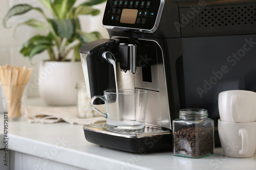 Modern coffee machine pouring milk into glass cup on white countertop in kitchen photo