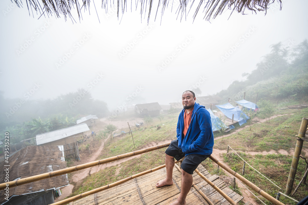 Asian fat traveler sitting on the wooden balcony with beautiful landscape and mist in the morning of Sapan Village nan Thailand.Sapan is Small and tranquil Village in the mountain. Asian fat traveler sitting on the wooden balcony with beautiful landscape and mist in the morning of Sapan Village nan Thailand.Sapan is Small and tranquil Village in the mountain.
