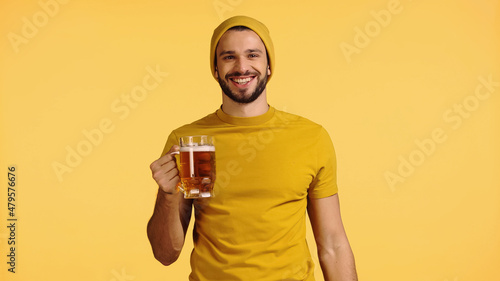 Foto happy man in beanie hat and t-shirt holding glass mug with beer isolated on yell