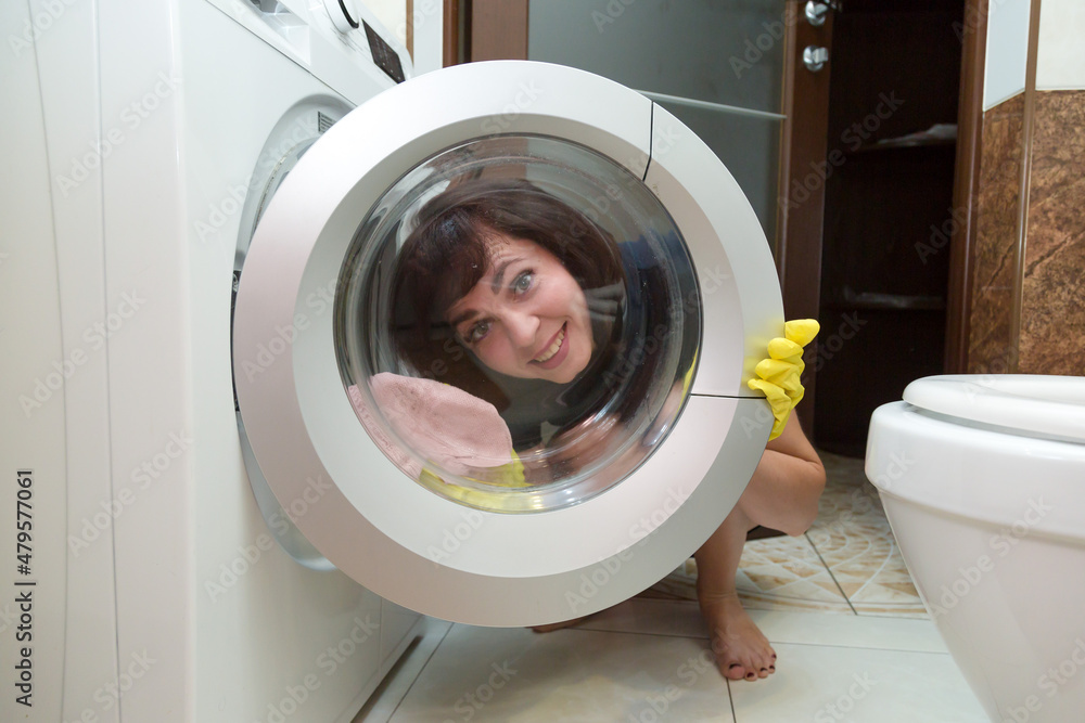 A smiling woman in yellow rubber gloves washes glass in a washing machine. A smiling woman in yellow rubber gloves washes glass in a washing machine.