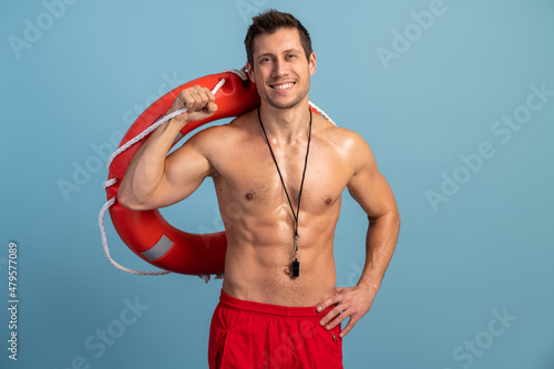Attractive, beautiful model with a lifebuoy at his shoulder posing on an blue background. Smiling man on a background of blank wall