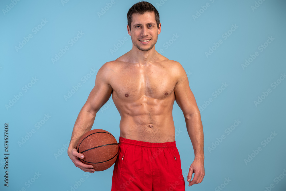 Waist up portrait view of the young man posing with ball over blue isolated background while playing basketball Waist up portrait view of the young man posing with ball over blue isolated background while playing basketball
