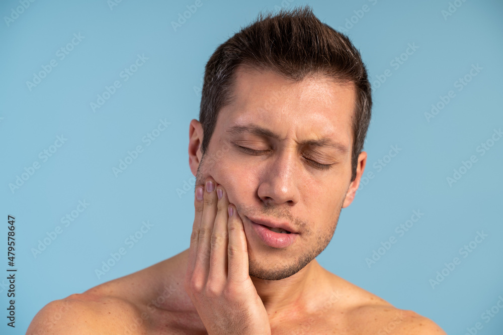 Obraz premium Young handsome man standing over isolated blue background touching mouth with hand with painful expression because of toothache or dental illness on teeth