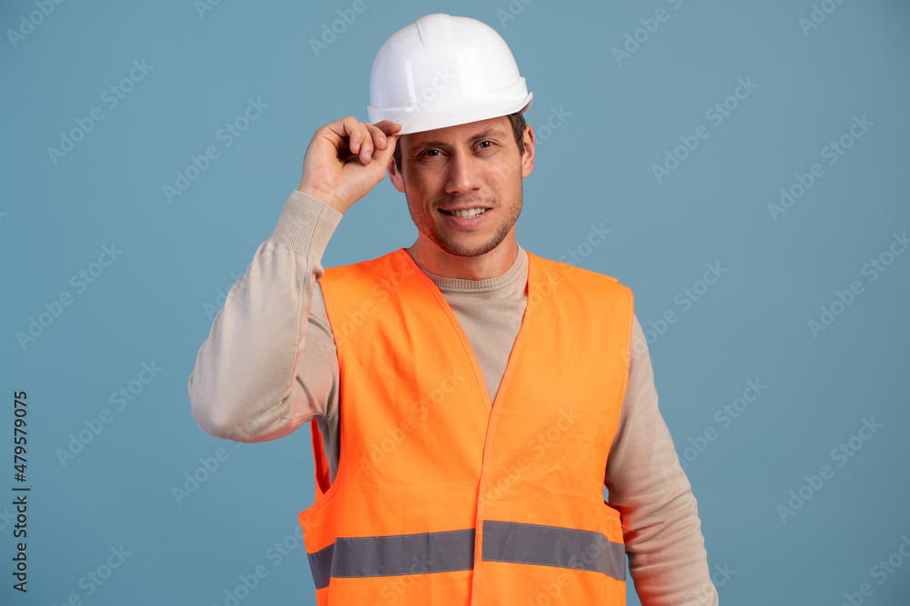 Smiling construction engineer posing with light smile in helmet at his head isolated over light blue background. Stock photo Smiling construction engineer posing with light smile in helmet at his head isolated over light blue background. Stock photo