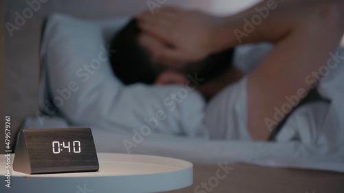 Clock on bedside table near blurred man on bed at night.