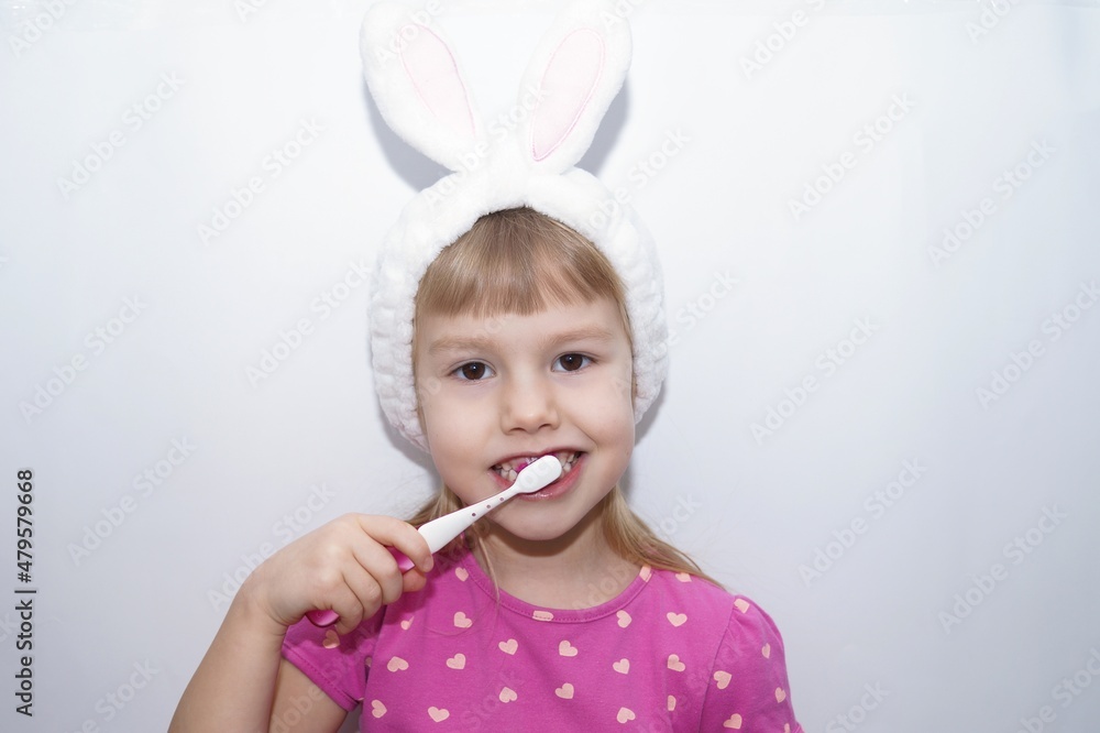 A little charming girl in a striped T-shirt is brushing her teeth with a bright children's toothbrush. Looks at the camera. White bandage on head. A little charming girl in a striped T-shirt is brushing her teeth with a bright children's toothbrush. Looks at the camera. White bandage on head.