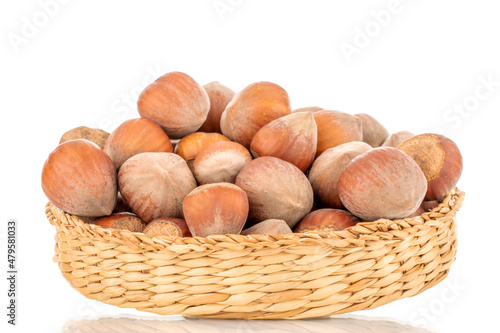 Several organic hazelnuts on a straw plate, close-up, isolated on white.