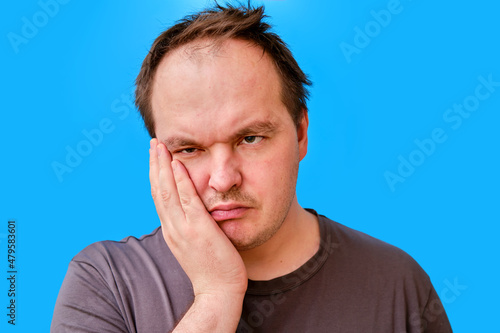 Portrait of a sad adult man with a disheveled appearance, blue studio background