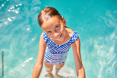A child on the steps climbing out of the pool, little girl having fun in the swimming pool, © bondarillia