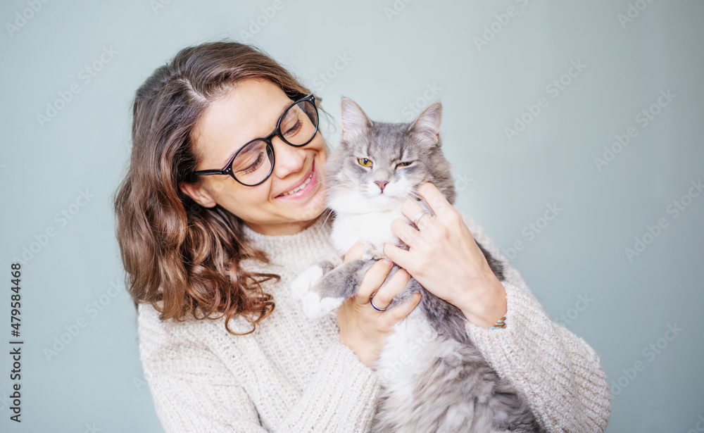 Young cheerful curly girl woman in eyeglasses holding a beautiful gray fluffy cat in her arms Young cheerful curly girl woman in eyeglasses holding a beautiful gray fluffy cat in her arms