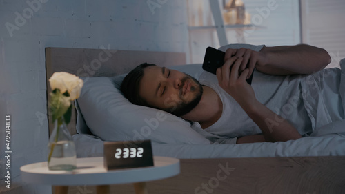Young man using smartphone on bed at night.