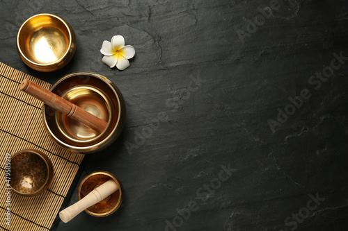 Flat lay composition with golden singing bowls on black table. Space for text