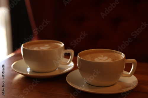 Cups of aromatic coffee with foam on wooden table in cafe