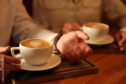Couple with cups of aromatic coffee at wooden table  closeup