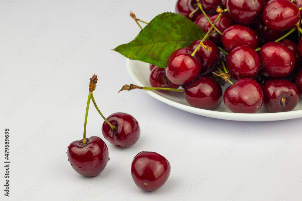 Ripe sweet cherries on a white plate on white background. Close up image. Ripe sweet cherries on a white plate on white background. Close up image.