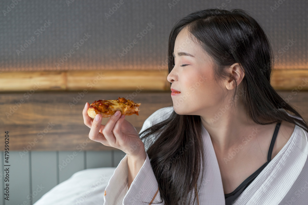 Happy young woman enjoy eating pizza on bed in hotel room. Beautiful female sitting in hotel bed eating pizza. Young woman hanging out eating pizza. Happy young woman enjoy eating pizza on bed in hotel room. Beautiful female sitting in hotel bed eating pizza. Young woman hanging out eating pizza.
