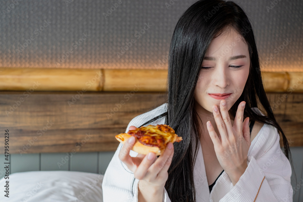 Happy young woman enjoy eating pizza on bed in hotel room. Beautiful female sitting in hotel bed eating pizza. Young woman hanging out eating pizza. Happy young woman enjoy eating pizza on bed in hotel room. Beautiful female sitting in hotel bed eating pizza. Young woman hanging out eating pizza.