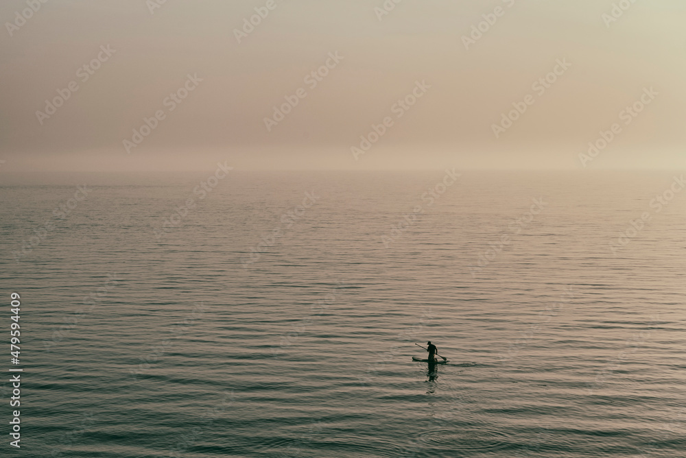 Fototapeta premium Silhouette of a man paddle boarding on the sea during sunset