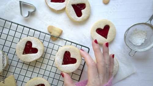 Top down view a person takes a bite from a Linzer Cookie. Heart shape raspberry jam filled biscuits. White background with modern and contemporary style. 4k real time motion. Romantic food concept