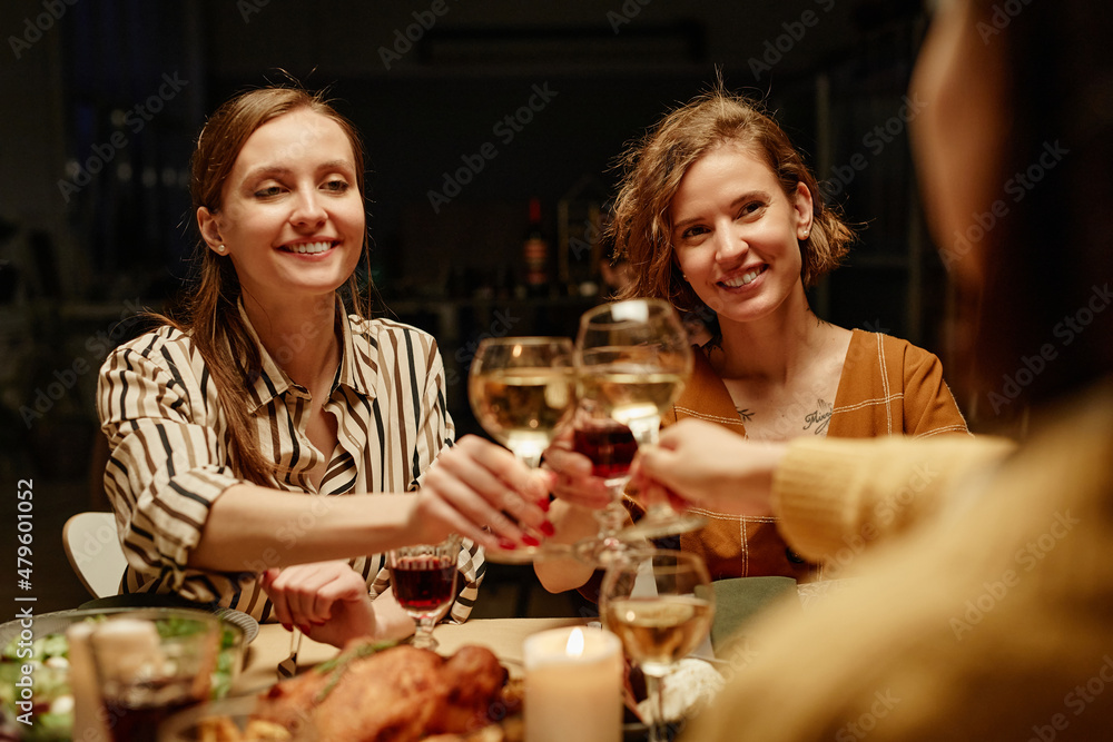 Happy young women toasting with wine and celebrating each other with holiday sitting at dining table Happy young women toasting with wine and celebrating each other with holiday sitting at dining table