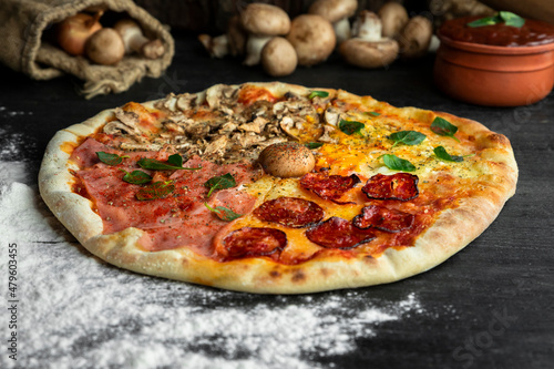 Italian Pizza Four Seasons (Pizza Quattro Stagioni) with different ingredients on the wooden table in the kitchen