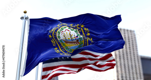 the flag of the US state of New Hampshire waving in the wind with the American flag blurred in the background