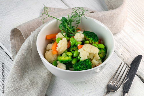 Mixed steamed vegetables in a white ceramic bow on wooden tablel. Vegan food - broccoli, carrots, beans, cauliflower and peas. photo