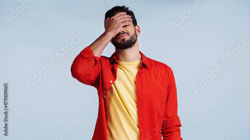 Bild auf Leinwand displeased and bearded man in red shirt doing face palm isolated on blue
