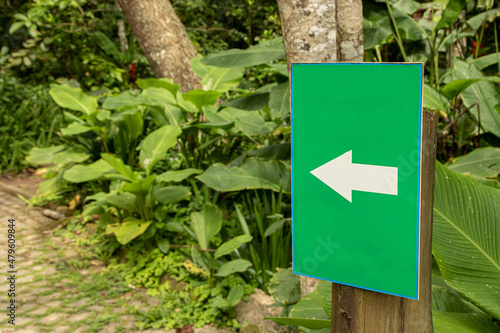 close de uma placa verde com seta branca apontando para vegetação tropical ao fundo photo