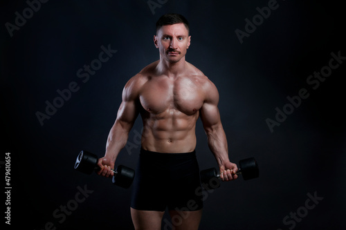 Professional bodybuilder performing biceps curls exercise with dumbbells over isolated black background. Studio shot of a male fitness model pumping iron. Close up, copy space.