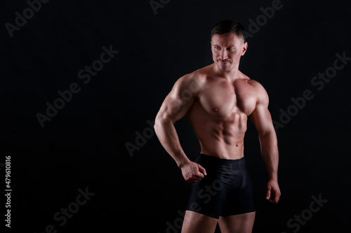 Professional bodybuilder posing over isolated black background. Studio shot of a fitness trainer flexing the muscles. Close up, copy space.