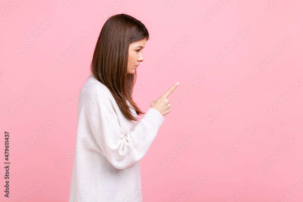 Side view portrait of strict female with raised finger, showing warning gesture, scolding somebody, wearing white casual style sweater. Indoor studio shot isolated on pink background. Side view portrait of strict female with raised finger, showing warning gesture, scolding somebody, wearing white casual style sweater. Indoor studio shot isolated on pink background.