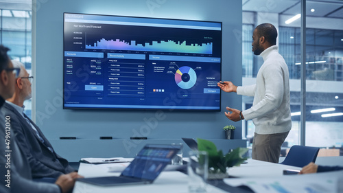 Diverse Modern Office: Motivated Black Businessman Leads Business Meeting with Managers, Talks, uses Presentation TV with Statistics, Charts, Big Data. Digital Entrepreneurs Work on e-Commerce Project