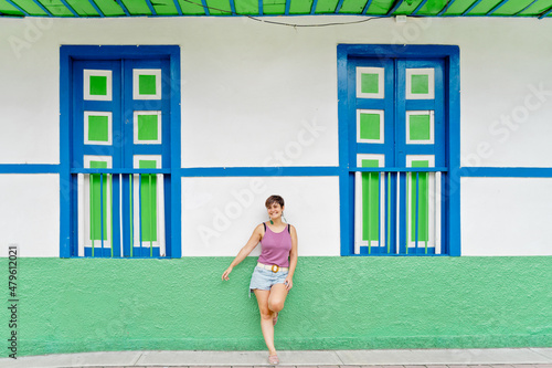 Panoramic full length view of woman standing against facade decorated with green and blue pattern. Horizontal view of latin american woman on colorful wall with summer clothes. Background concept