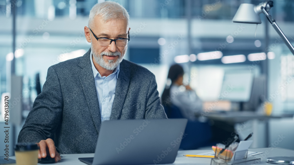 Modern Office: Portrait of Successful Middle Aged Bearded Corporate Businessman Working on a Laptop at his Desk, Smiling. Diverse Workplace with Professionals. Modern Office: Portrait of Successful Middle Aged Bearded Corporate Businessman Working on a Laptop at his Desk, Smiling. Diverse Workplace with Professionals.