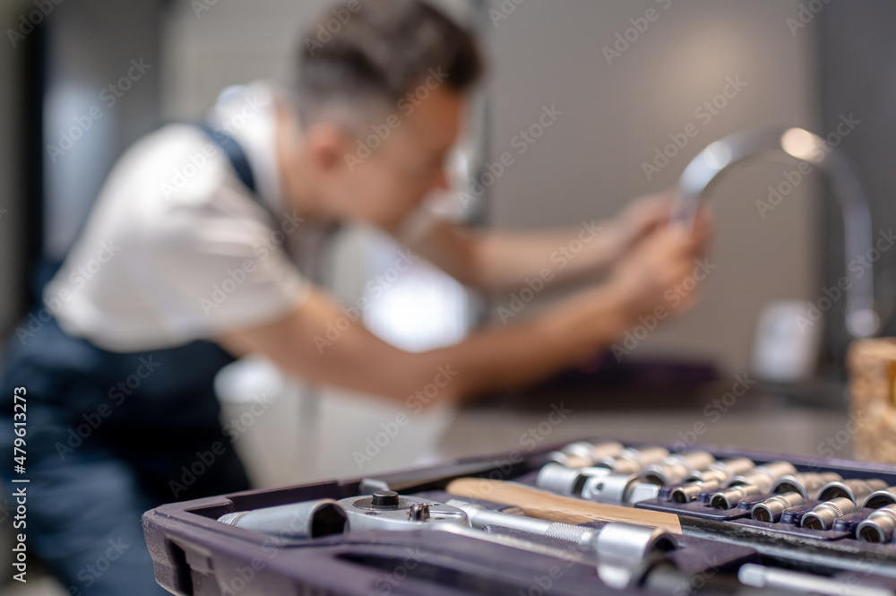 Tools in open case and man repairing water tap Tools in open case and man repairing water tap