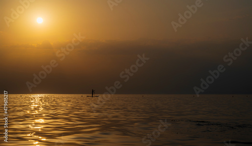 Silhouette of unrecognizable woman in wetsuit paddling on a SUP board. Female floating on a stand up paddle board in the gulf. Summer season and active leisure concept. Dynamic recreation.