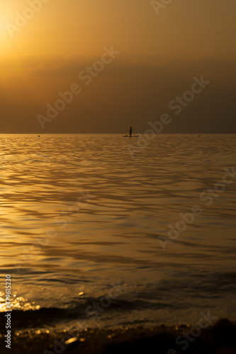 Silhouette of unrecognizable woman in wetsuit paddling on a SUP board. Female floating on a stand up paddle board in the gulf. Summer season and active leisure concept. Dynamic recreation.