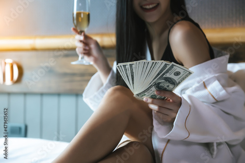 Rich girl holding a lot of money Beauty woman get celebrating with champagne that she can earn a lot of money in bed at hotel room She spend money She is rich person with happiness and smile face photo