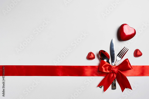 Fork, knife and spoon bowed with red ribbon on white background, concept of romantic lunch on Valentine's Day
