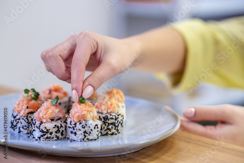Close up of sushi on the plate and womans hands putting topping