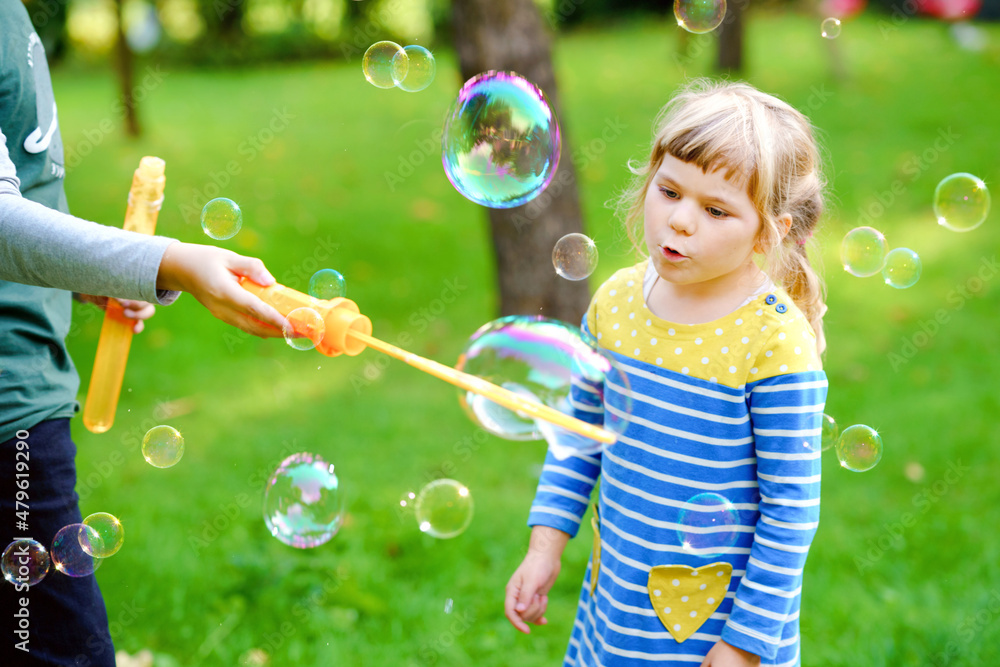 Happy little preschool girl and school kid boy having fun with blowing soap bubble blower. Children, lovely siblings playing together. Active funny healthy kids. Brother and sister in love.