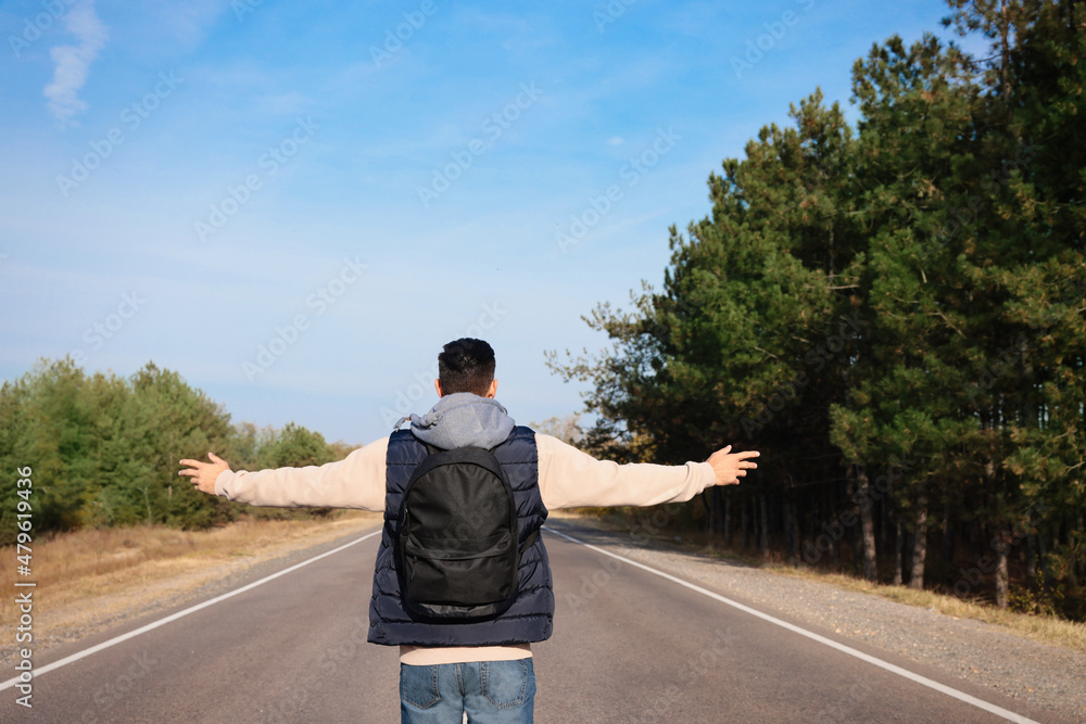 Man with backpack on road near forest, back view Man with backpack on road near forest, back view