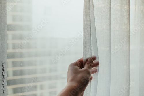 Person touching and holding a white curtain in room next to the window
