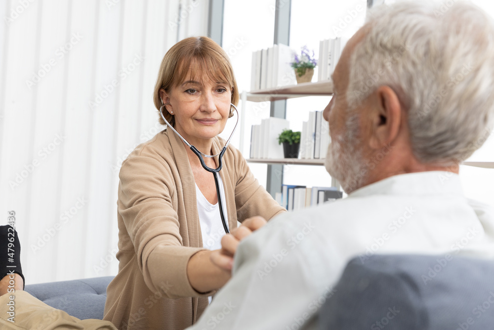 senior woman doctor on home visit and examining elderly man patient by stethoscope senior woman doctor on home visit and examining elderly man patient by stethoscope