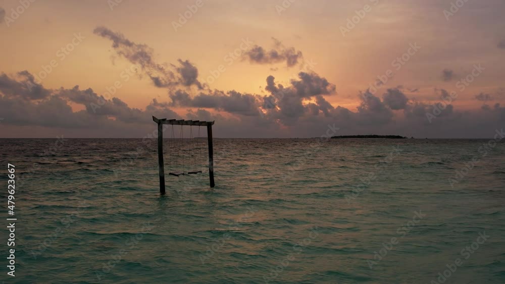 Gimbal shot of evening at tropical resort, picturesque sunset and island. Beautiful, panoramic skyline of ocean water and beach in Maldives with beach swing. Concept of trip Gimbal shot of evening at tropical resort, picturesque sunset and island. Beautiful, panoramic skyline of ocean water and beach in Maldives with beach swing. Concept of trip
