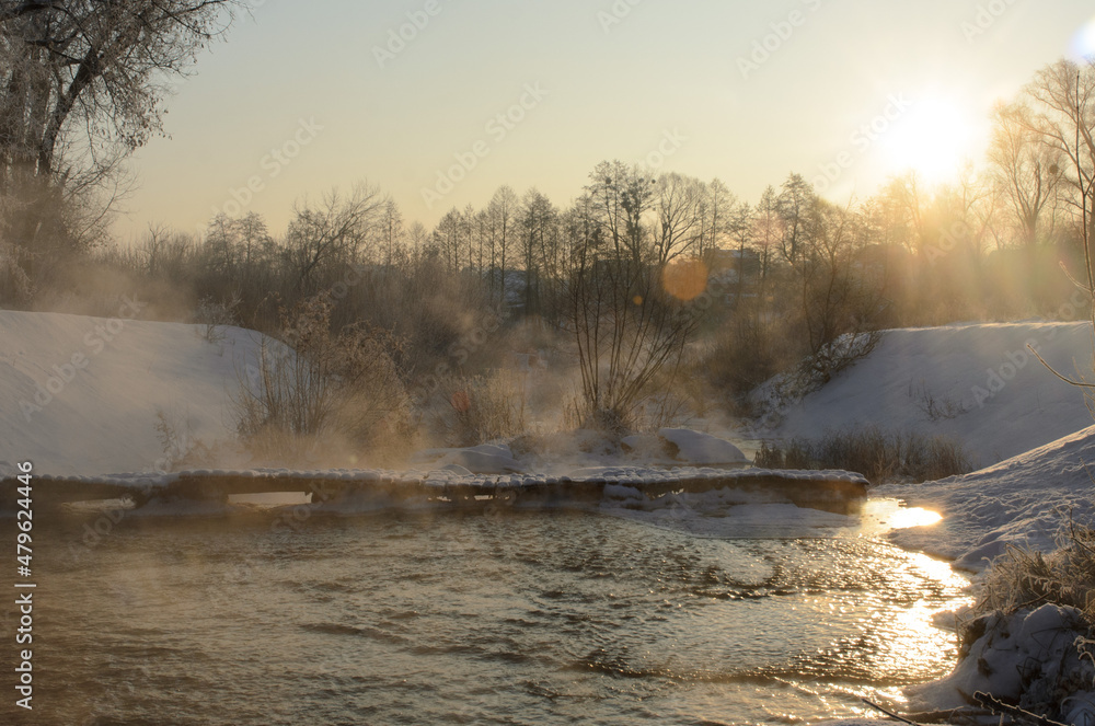 Dawn in winter, snow and blue on the trees, fog over the water.