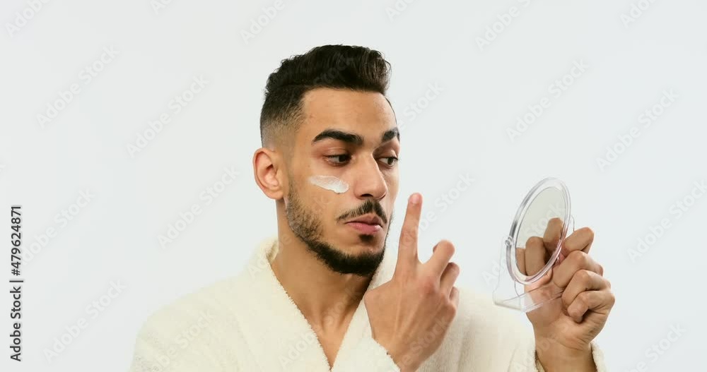 Man in bathrobe applying cream on face over white background Man in bathrobe applying cream on face over white background