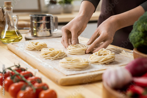 Hands of young creative woman preparing italian pasta on wooden board while standing by kitchen table