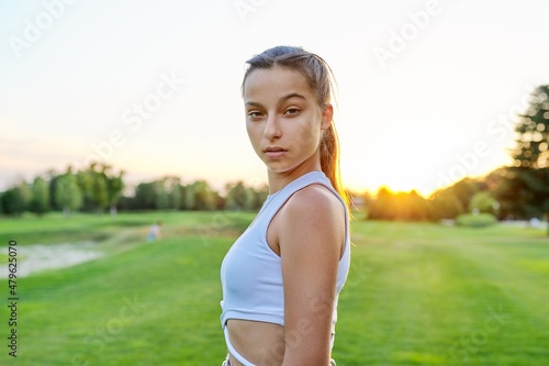 Serious teenage girl looking at the camera, in the park on lawn. photo